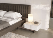 Modern bedroom with a bed and nightstand featuring a lamp.