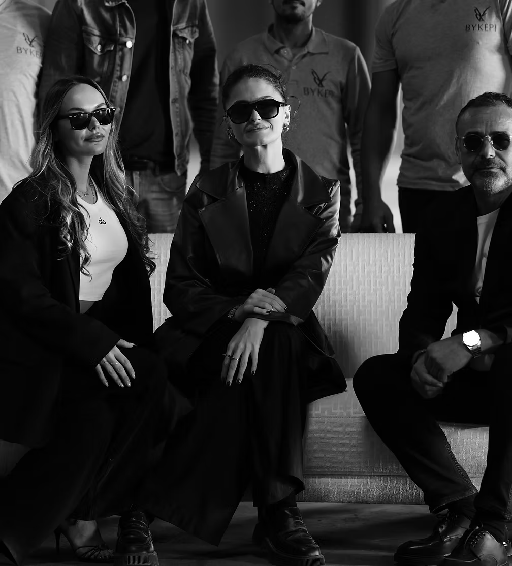 Black and white photo of three people sitting together, wearing sunglasses and formal attire.